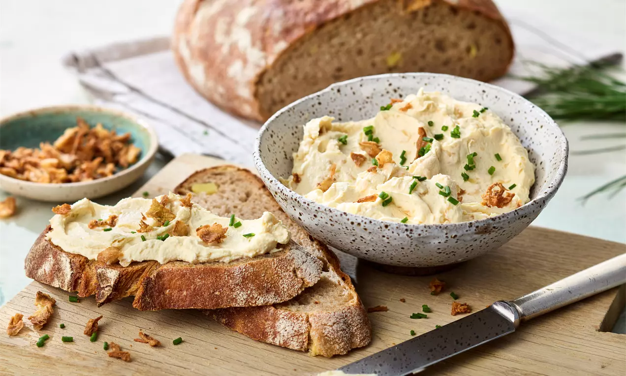 Cremiger Zwiebel-Dip in einer gesprenkelten Schale, garniert mit knusprigen Röstzwiebeln und Schnittlauch, daneben frisches Bauernbrot