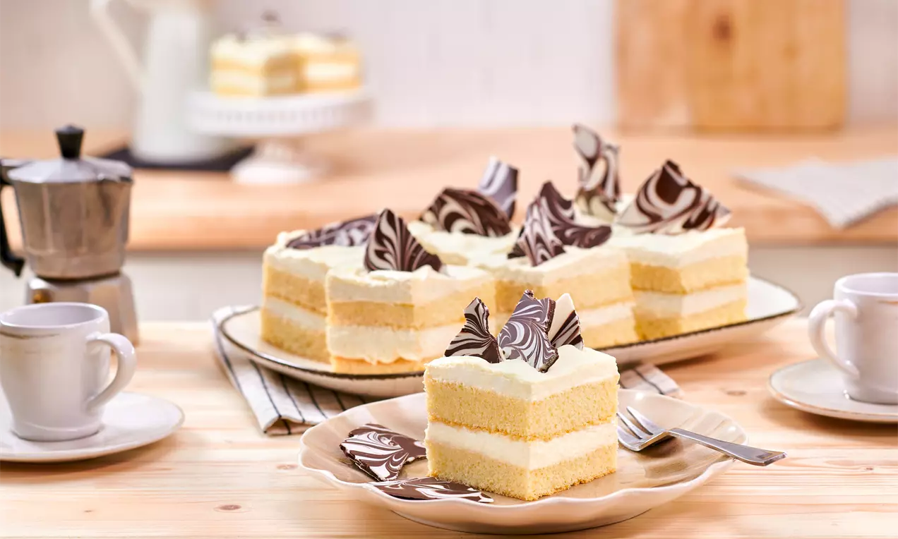Mascarpone-Schnitten mit hellgelben Schichten und weißer Creme, dekoriert mit marmorierten Schokoladsplittern auf beige Teller angerichtet