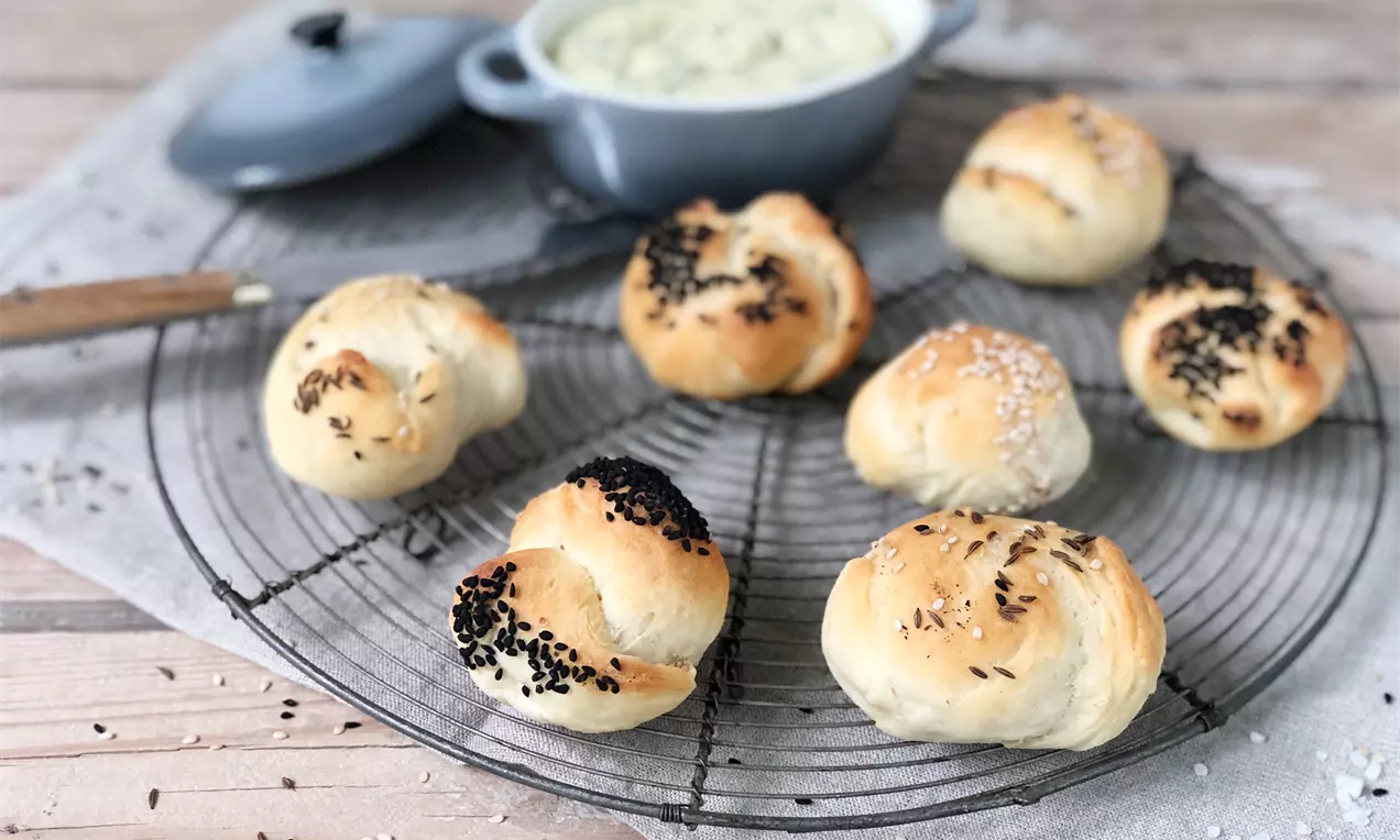 Goldbraune Quark-Öl-Teig-Brötchen mit glänzender Oberfläche, teils bestreut mit Sesam oder Schwarzkümmel, auf einem runden Gitter aus Draht