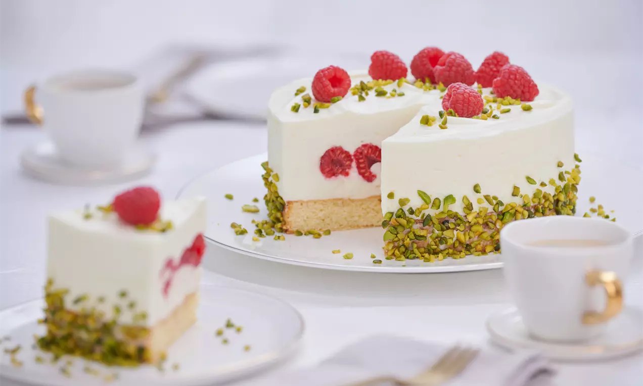 Pistazien-Himbeer-Torte mit hellgrüner Pistaziencreme, roter Himbeerfüllung, Joghurt-Sahnetopping, Himbeeren und gehackten Pistazien
