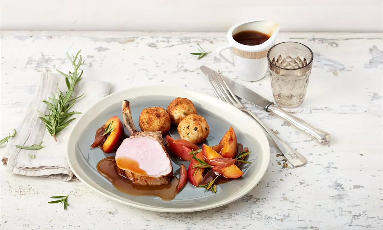 Zartrosa Duroc-Schweinkarree auf brauner Sauce, angerichtet mit goldbraunen Risottobällchen und glänzenden Nektarinenstücken auf weißem Teller