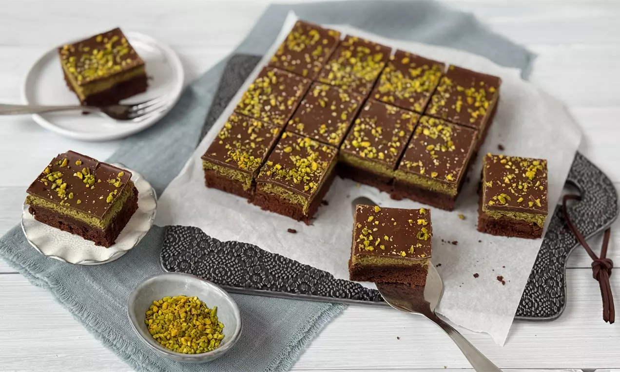 Dubai Brownie mit saftiger Schokolade, glänzender Glasur, gehackten grünen Pistazien und goldenen Kadayif-Fäden auf weißem Teller
